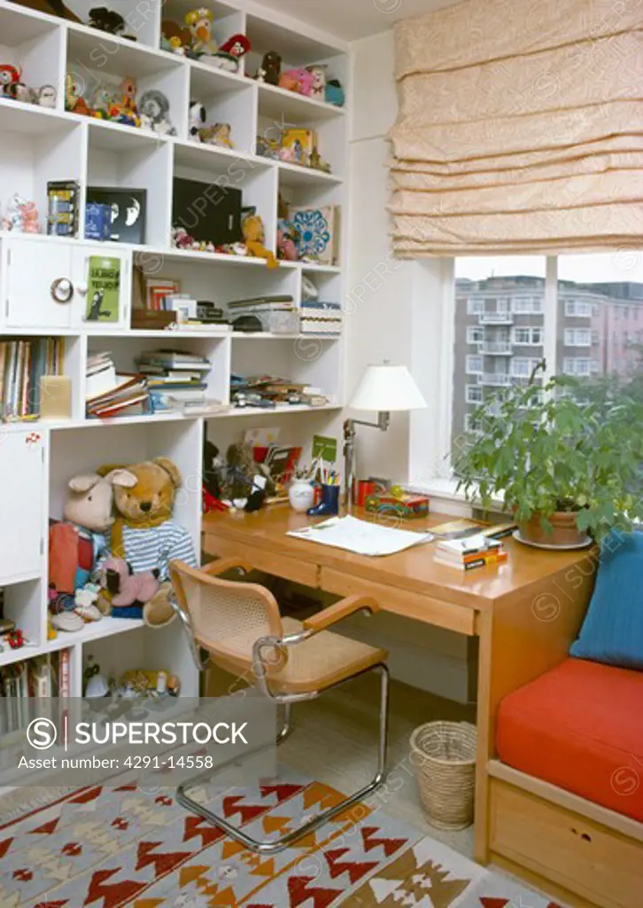 Wall-to-ceiling cube shelving in study bedroom with chair and small wooden desk in front of window with cream blind