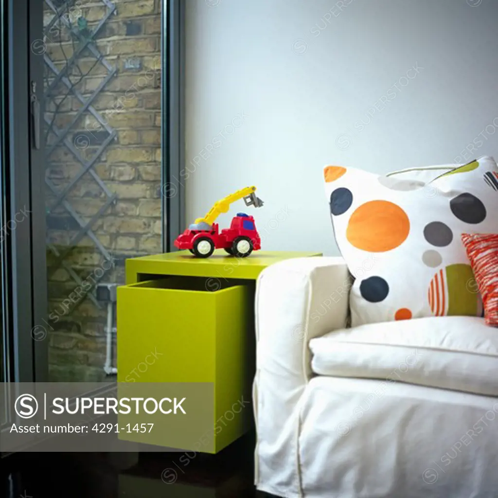 Red toy truck on lime green table with pull out storage drawer beside spotted cushion on white sofa in modern living room