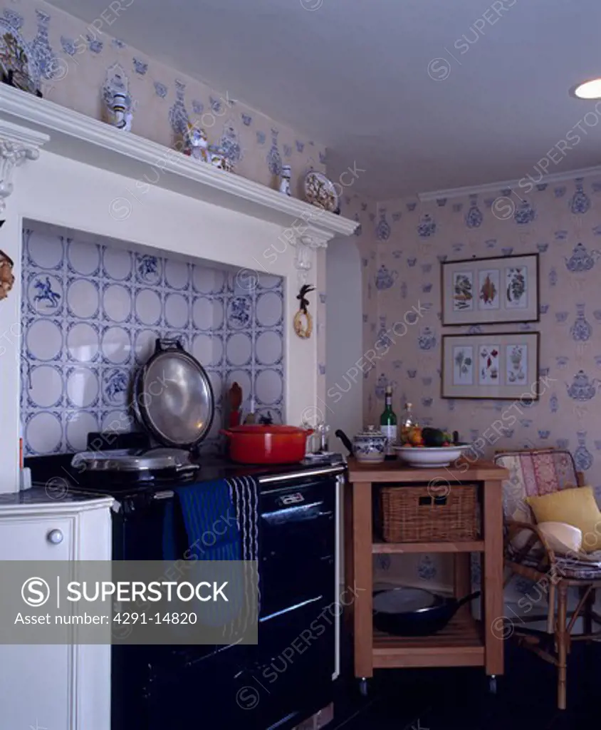Blue and white tiled wall behind black Aga oven in country kitchen with butcher's block and teaspot-patterned wallpaper