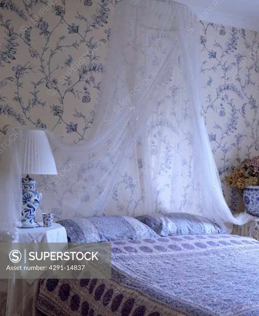 White voile drapes above bed with blue and white Indian bedspread and pillows in bedroom with blue and white wallpaper