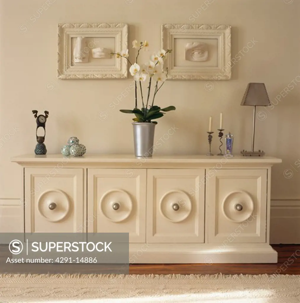 White orchid in metal pot on white painted sideboard concealing television