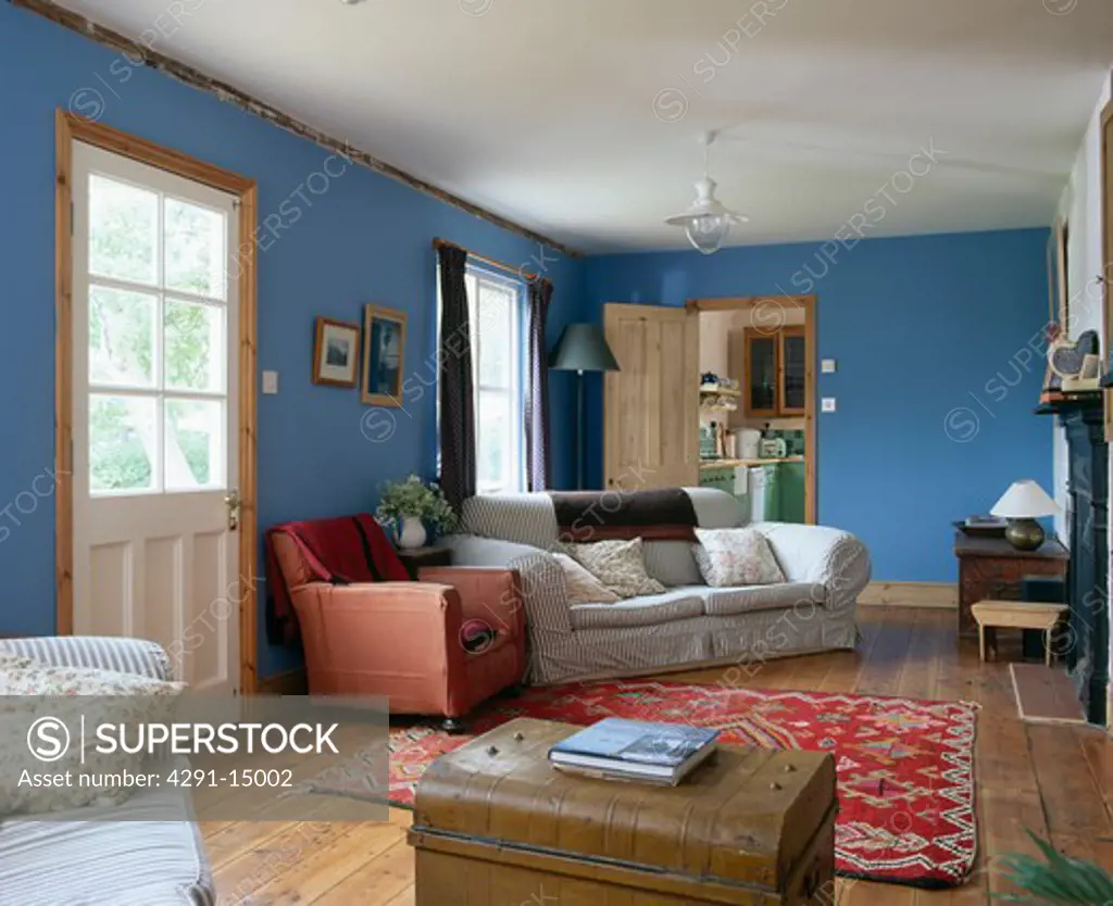 Striped sofas and old chest in blue country living room with oriental rug on wooden flooring