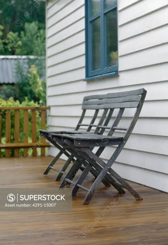 Folding black wooden chairs on decking in front of white ship-lap house