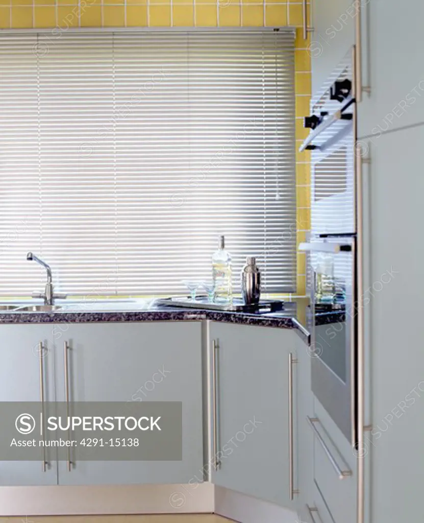 Metallic slatted blind above sink in modern kitchen with pale grey units