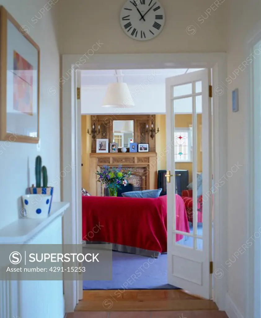 Circular clock above glazed double doors open to living room with red sofa