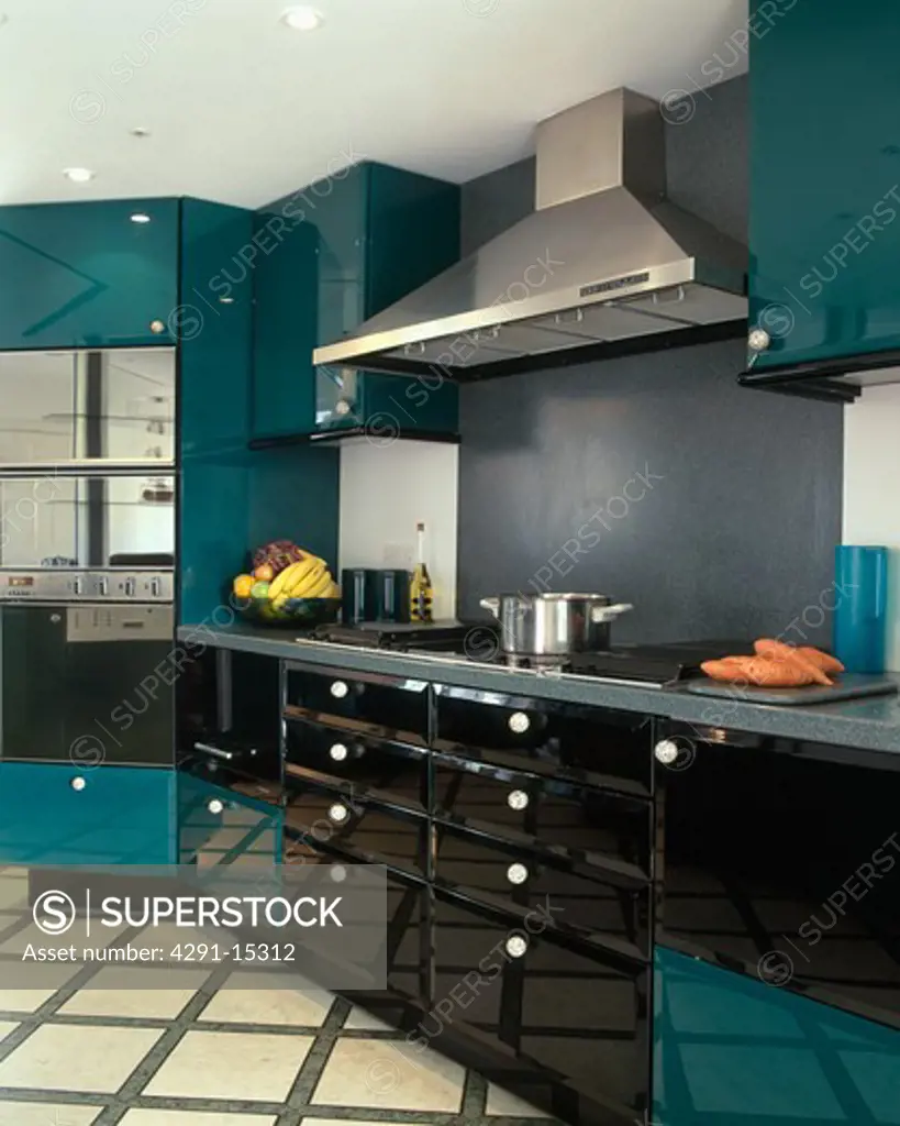 Stainless steel extractor above hob in modern kitchen with green and black units