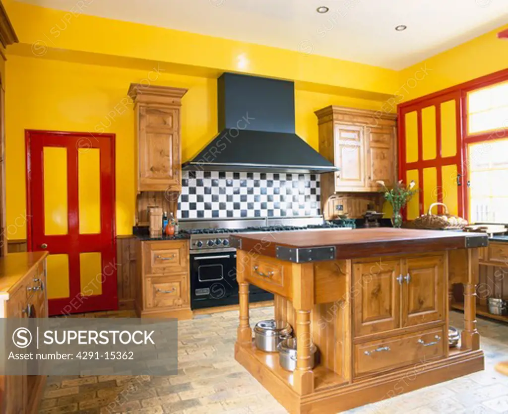 Large wooden island unit in yellow kitchen with red paintwork and brick flooring