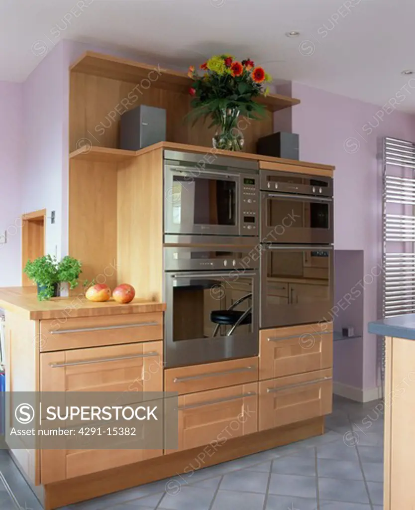 Stainless steel double ovens in pale wood unit in modern mauve kitchen