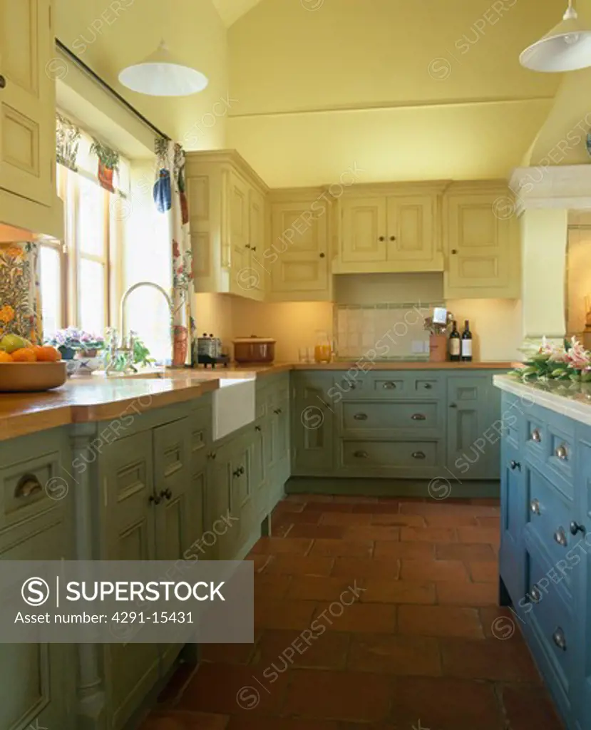 Quarry floor tiles in pastel yellow kitchen with blue and green painted wooden units