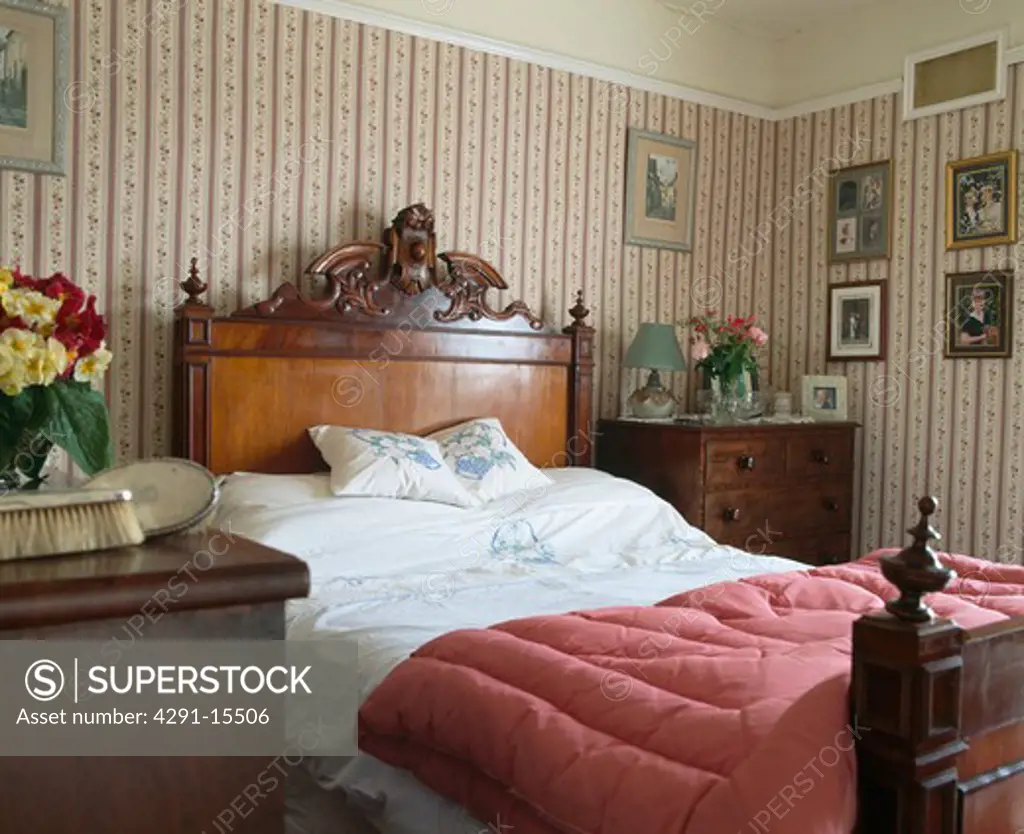 Old-fashioned pink eiderdown on antique mahogany bed in country bedroom with patterned wallpaper