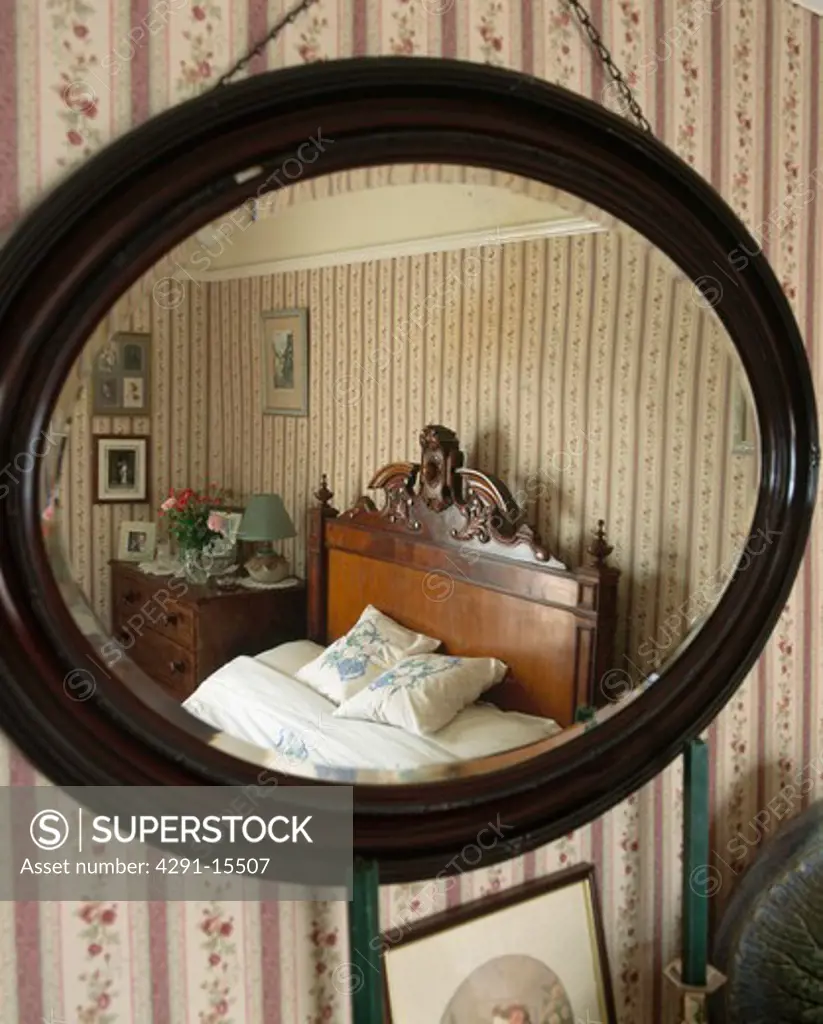 Close-up of oval mahogany-framed mirror with reflection of old-fashioned country bedroom