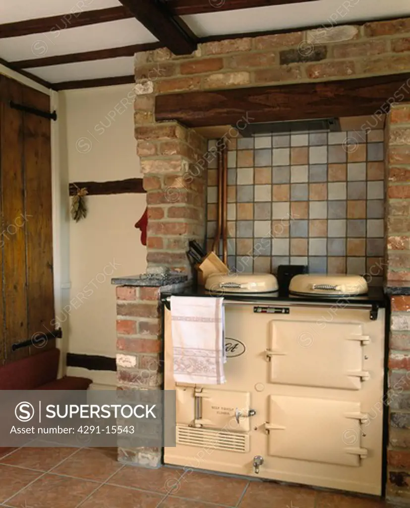 Ceramic wall tiles above cream Aga oven in brick fireplace in cottage kitchen