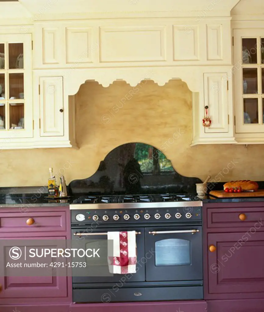 Close-up of black range oven in purple fitted unit below fitted cream cupboard in country kitchen