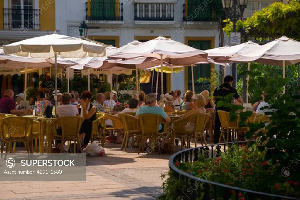 People sitting at tables under parasols at outdoor restaurant in Spain