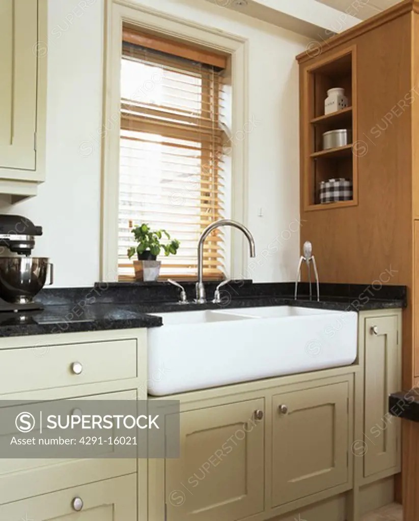Double Belfast sink below window with slatted wooden blind in modern cream kitchen