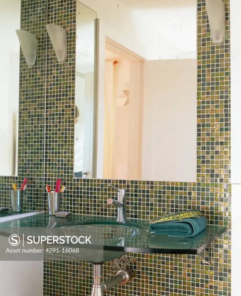 Close-up of large mirror above glass basin in modern bathroom with green and gold metallic mosaic tiles