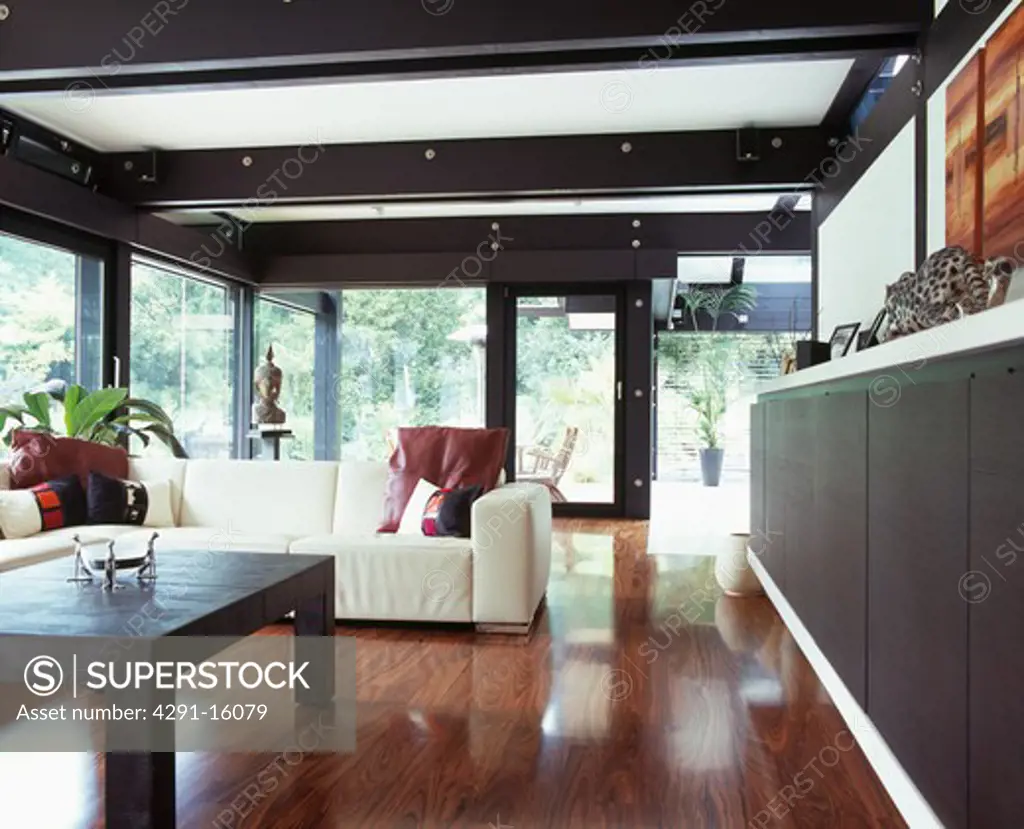 Polished wooden flooring in large modern living room with white sofa and black ceiling beams