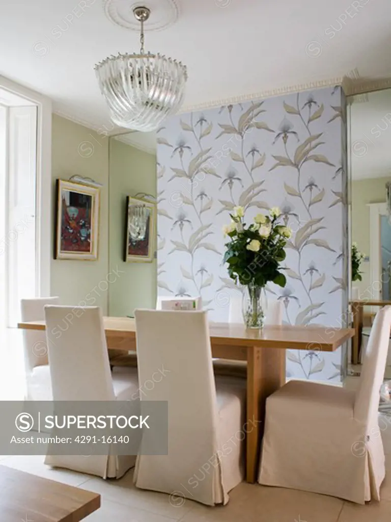Beige loose-covers on chairs at wooden table in modern pale green dining room with panel of wallpaper