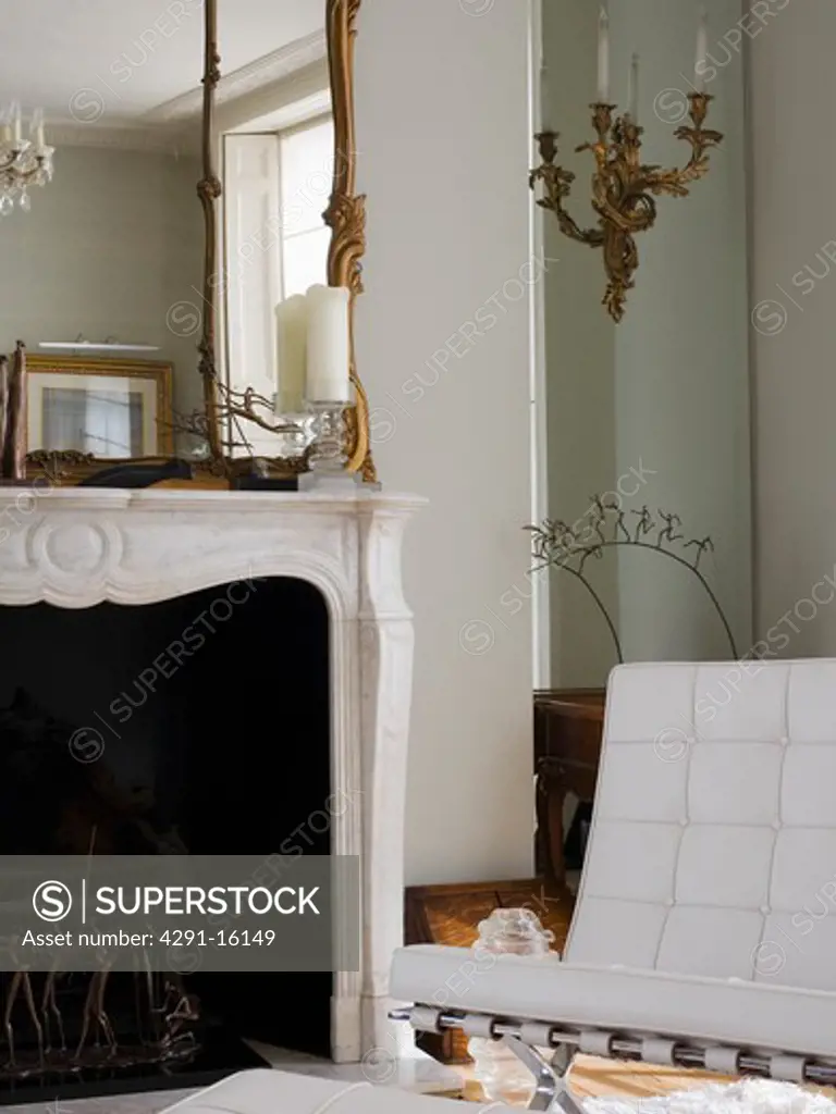 White Mies van der Rohe Barcelona chair beside marble fireplace with antique overmantel mirror