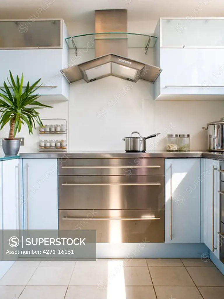 Stainless-steel and glass extractor above stainless-steel range oven in modern white kitchen with pastel blue units