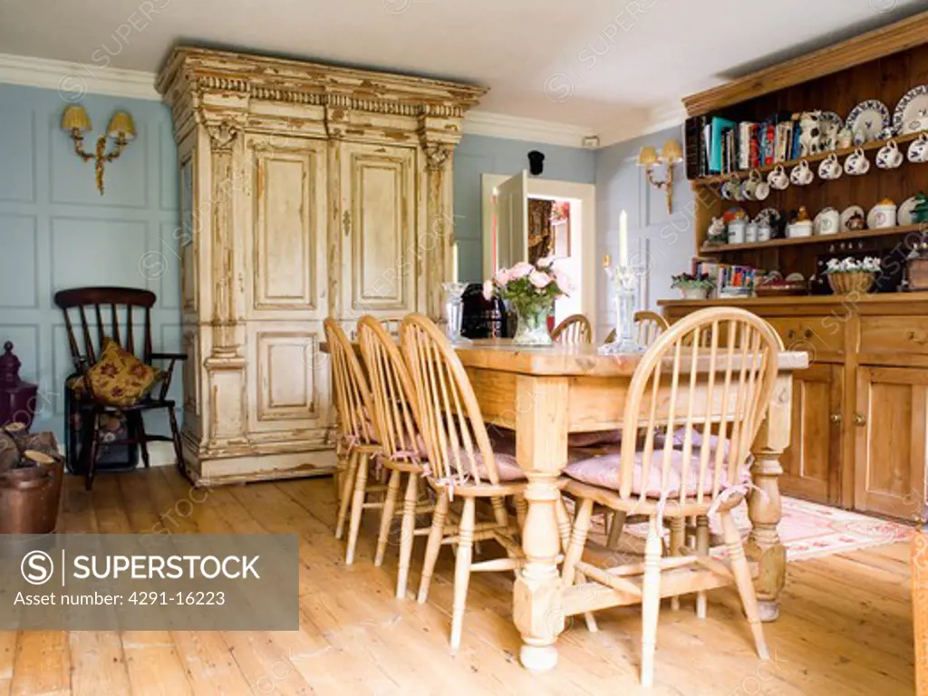 Windsor chairs and wooden table in pale blue country dining room with large ornate cream cupboard and pine dresser