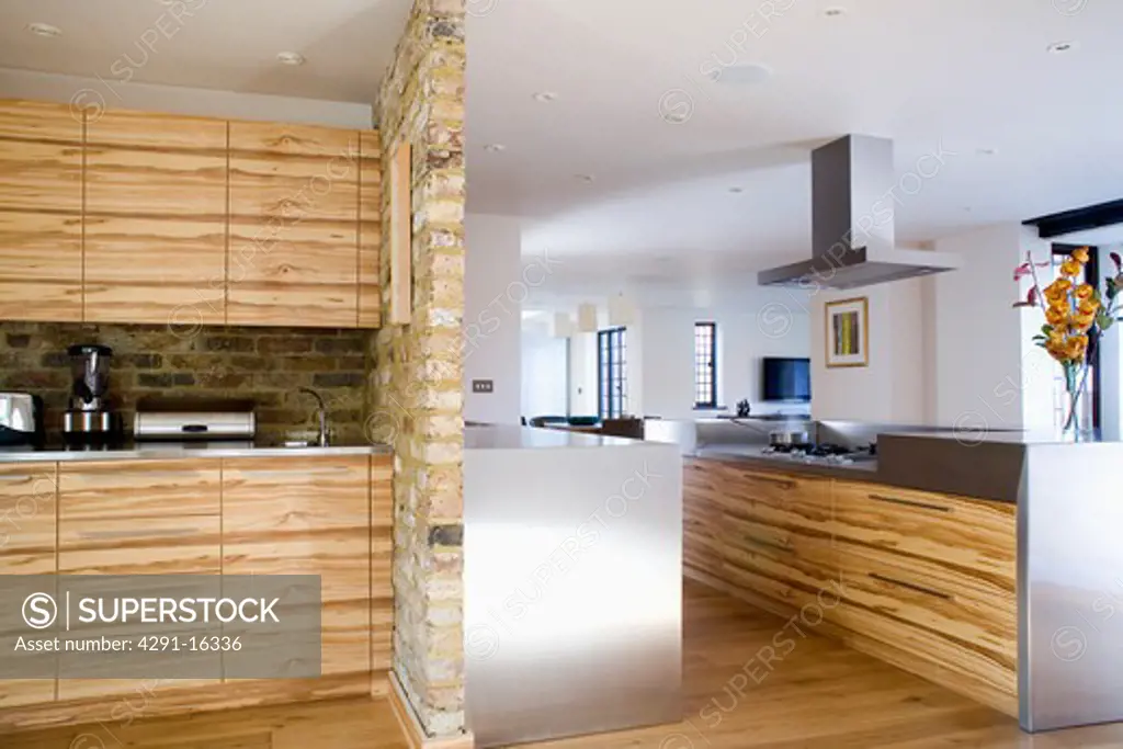Stone-clad dividing wall in modern white kitchen extension with pale wood and stainless steel fitted units
