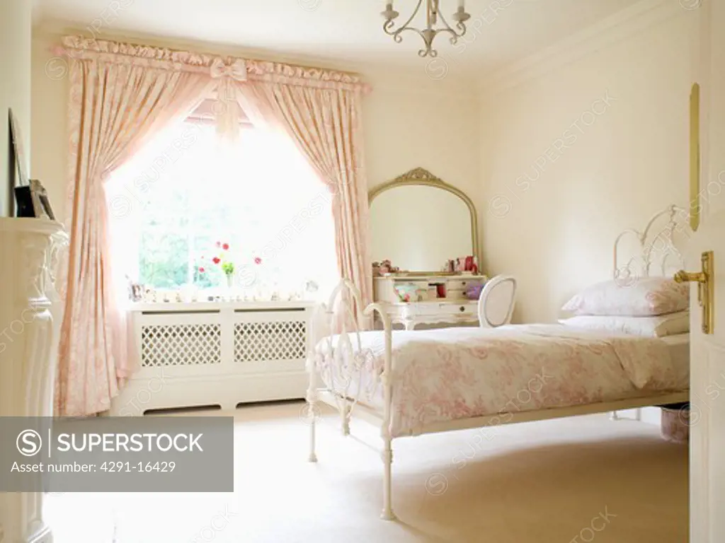Pink Toile-de-Jouy curtains and bedlinen in cream country bedroom with cream carpet and wrought-iron bed