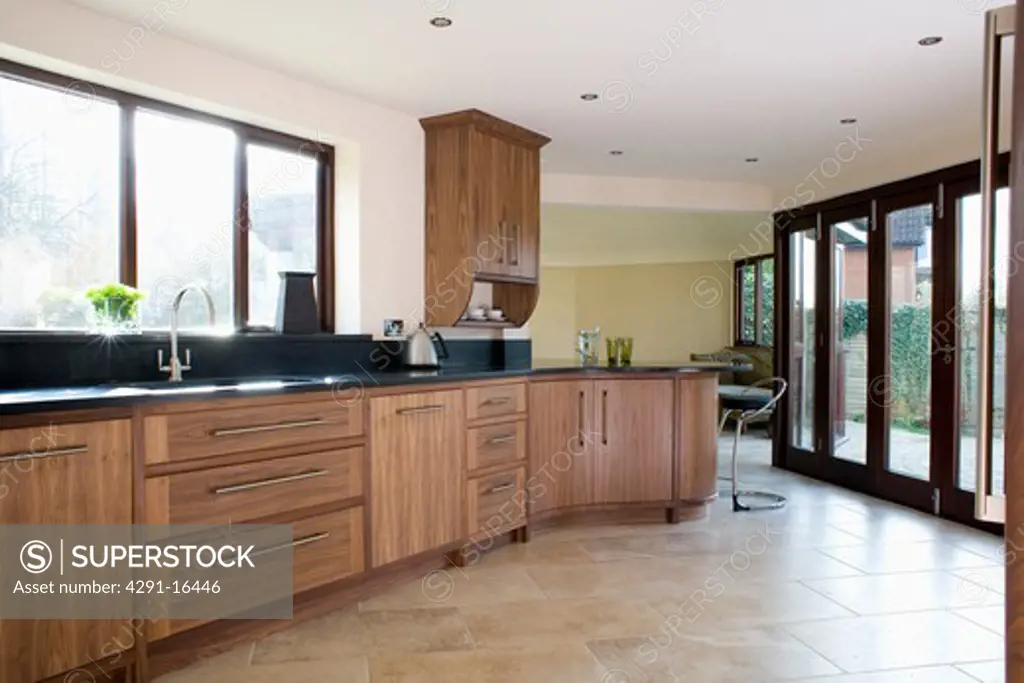 Limestone flooring and glass patio doors in modern kitchen with fitted walnut units