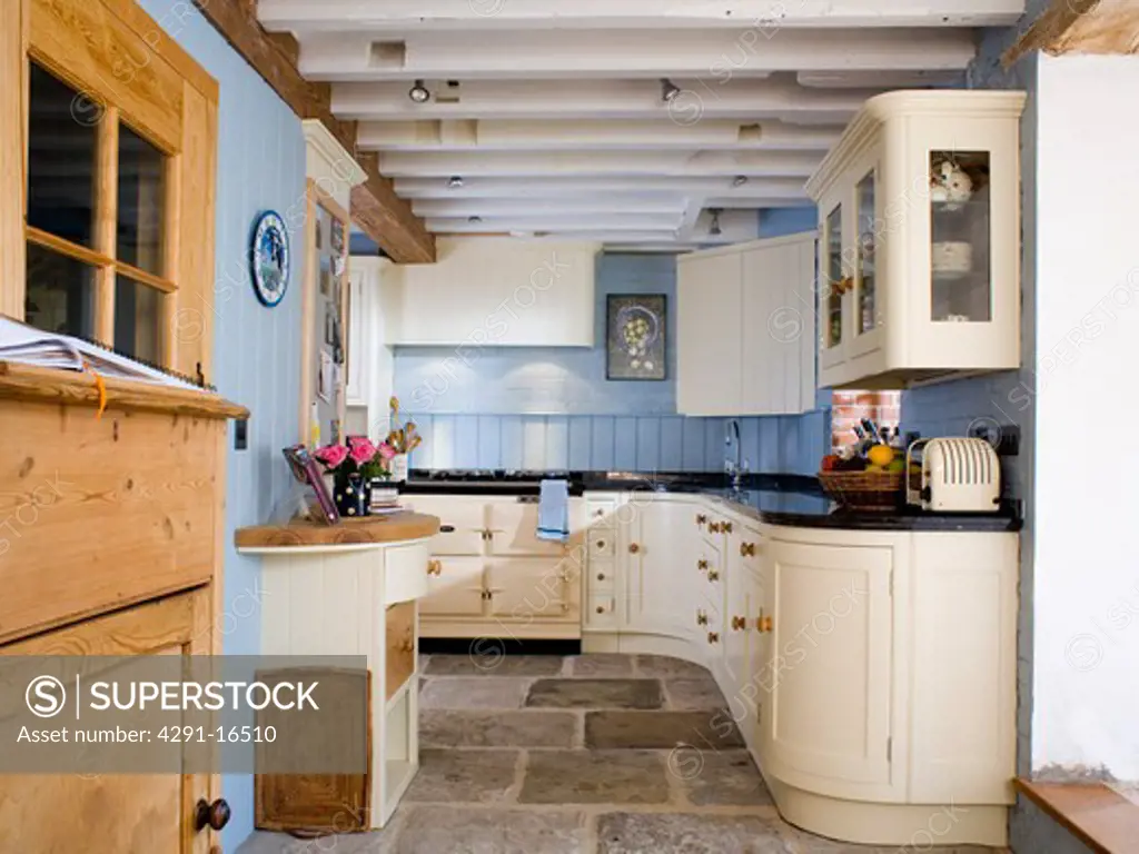 Fitted cream units and flagstone floor in pastel blue country kitchen