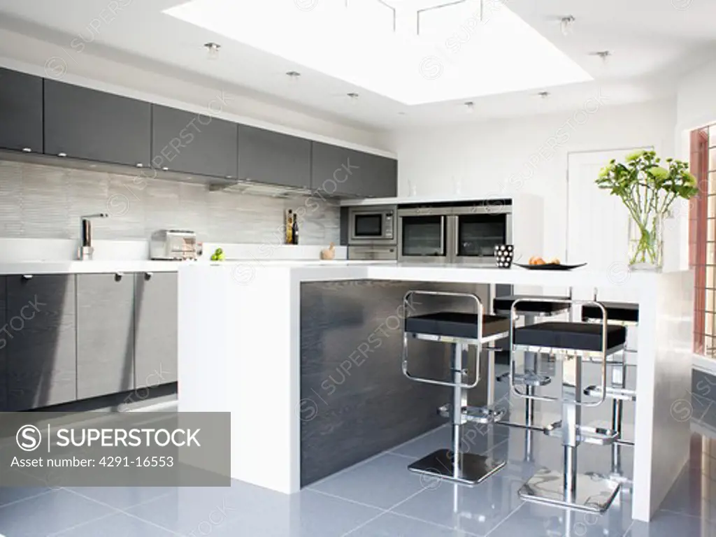 Black and chrome stools at breakfast bar on island unit in modern monochromatic kitchen