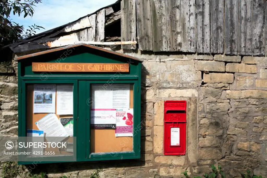 Village parish noticeboard and red postbox in stone wall