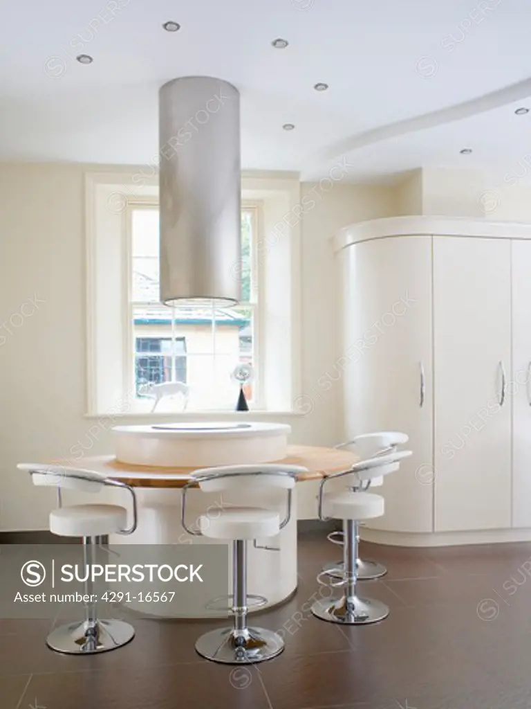 Cylindrical extractor above hob set in circular island unit with breakfast bar and white and chrome stools