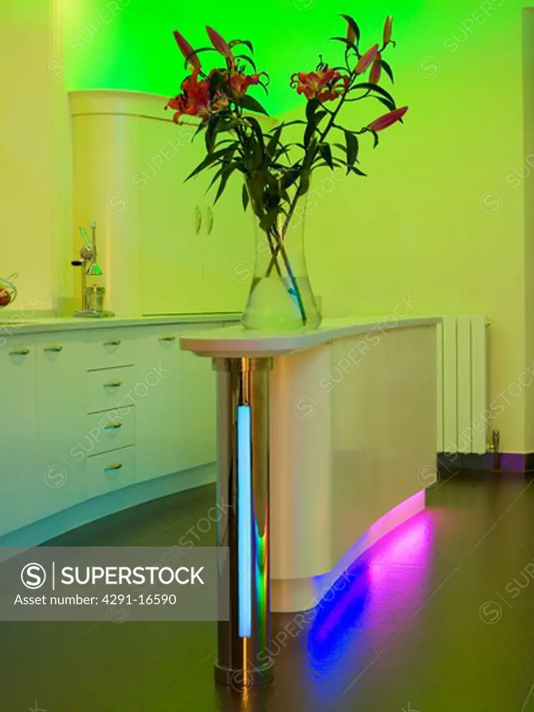 Purple and blue fluorescent lighting below island unit in modern kitchen with green uplighting
