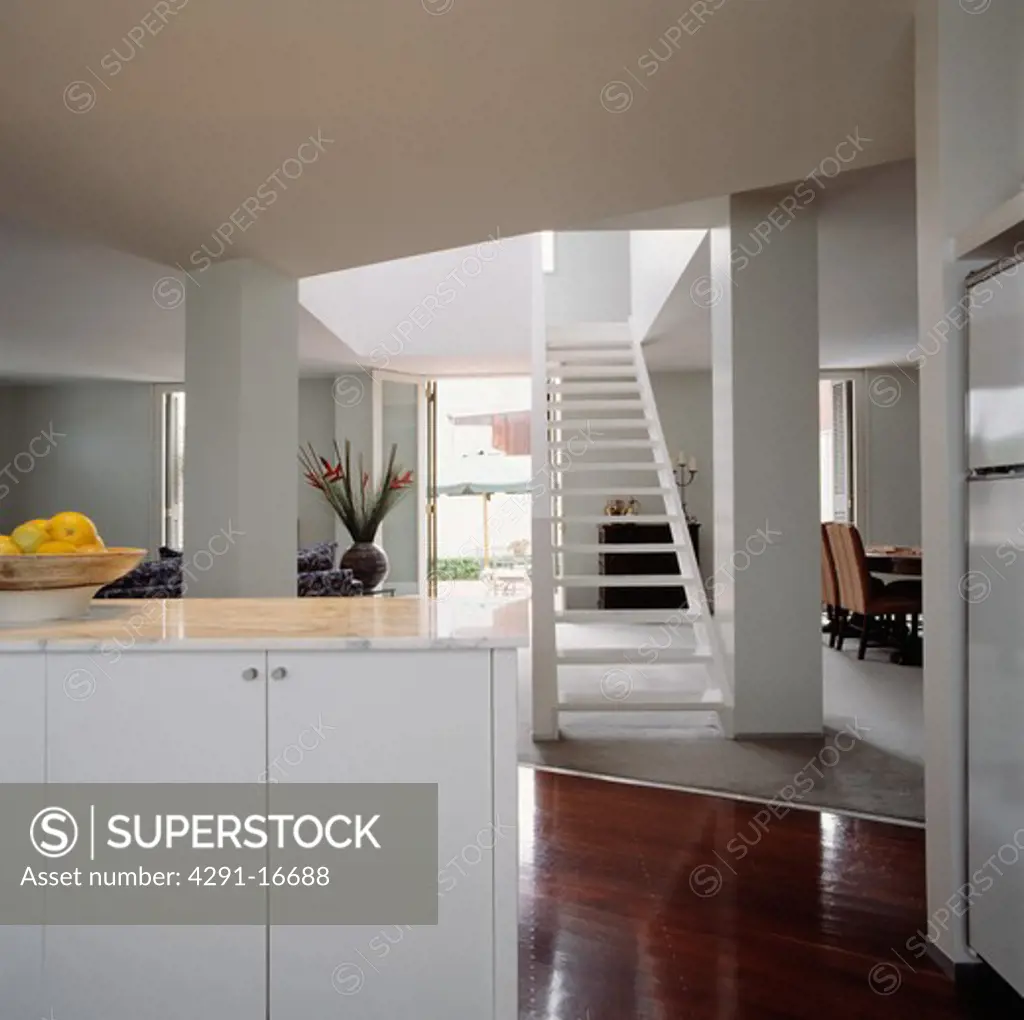 Modern white openplan hall kitchen with white open-tread staircase and polished wooden flooring