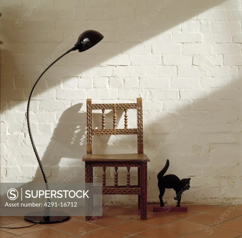 Black floor lamp and carved wooden chair against white painted brick wall