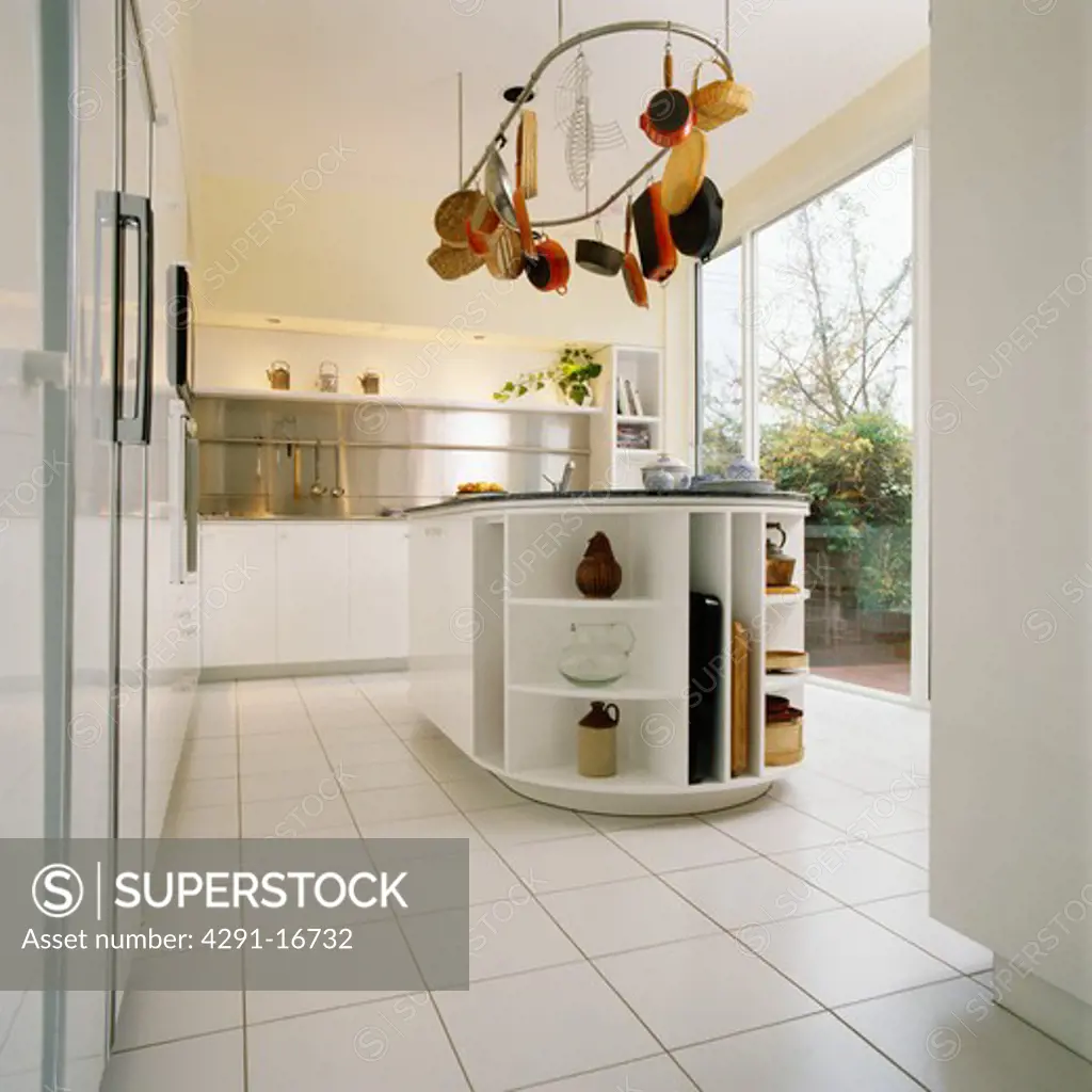 White ceramic tiled floor in modern white kitchen with pans on rack above island unit