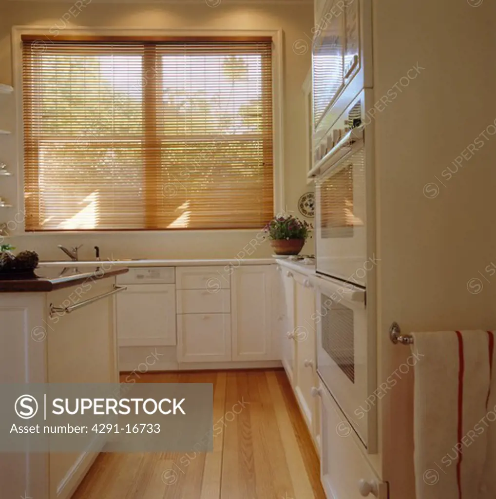 Slatted wooden blind and wooden flooring in modern white kitchen