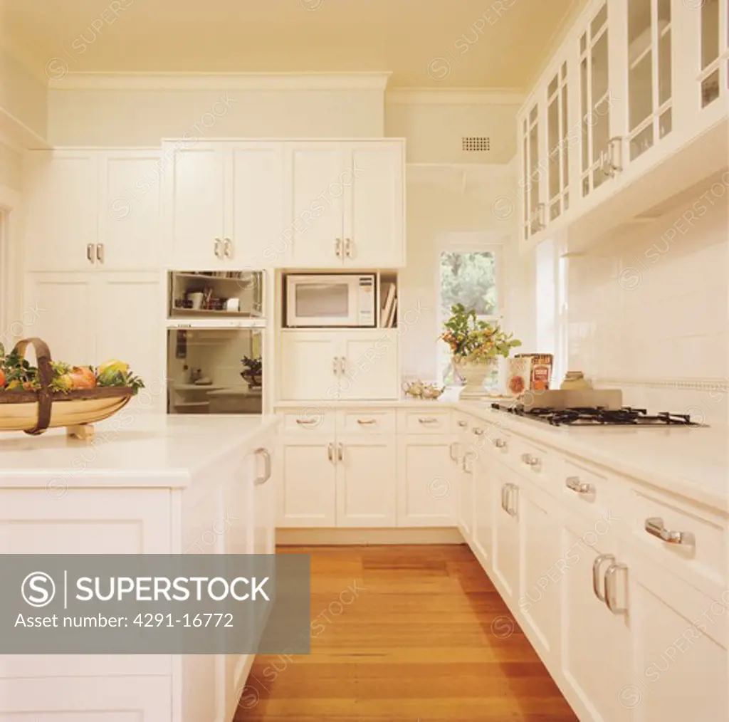 Wooden flooring in large white kitchen with painted wood fitted cupboards