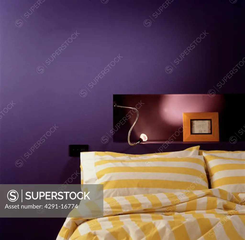 Yellow and white striped pillows and duvet on bed below light on alcove shelf in modern purple bedroom