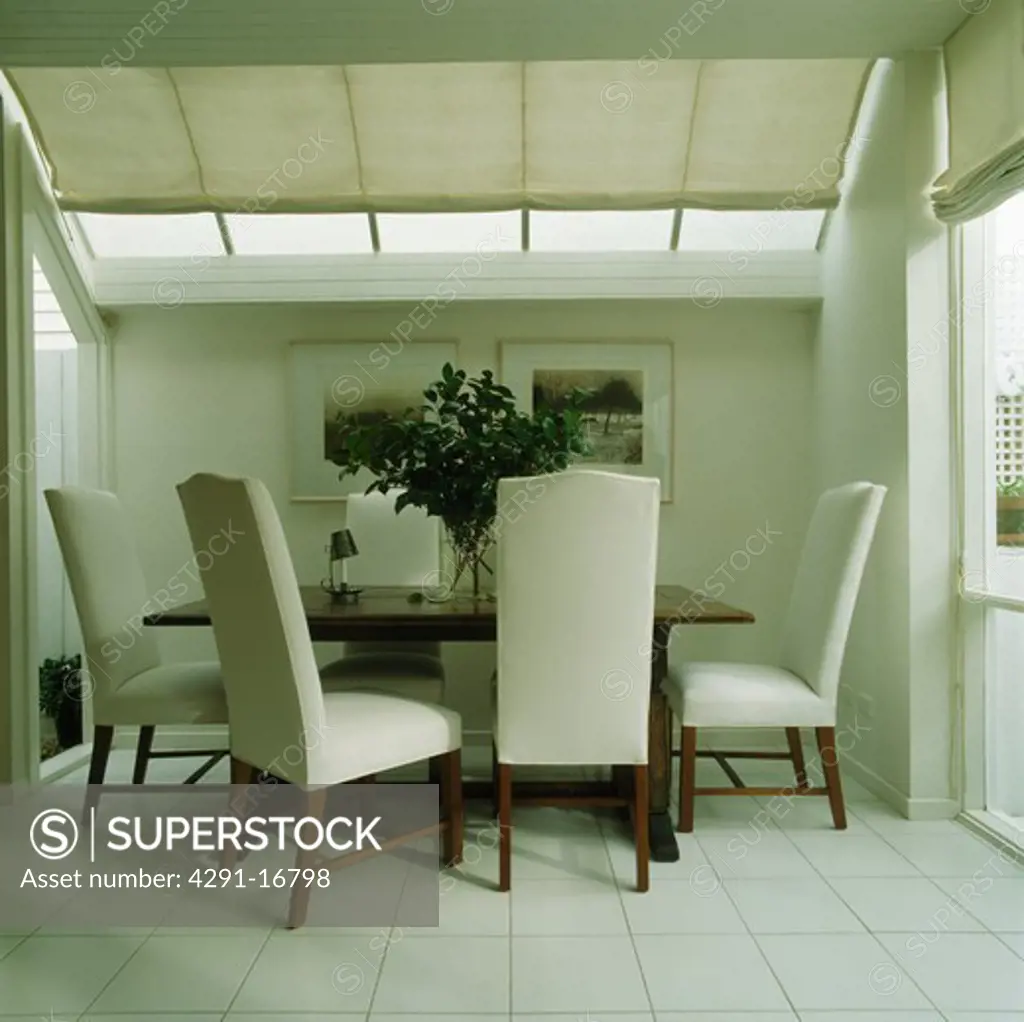 White upholstered chairs in modern white dining room with white ceiling blind