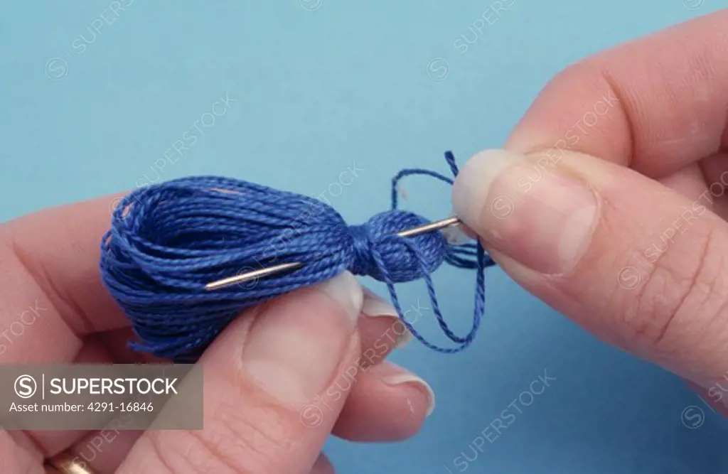 Close-up of hands holding needle and skein of blue cotton