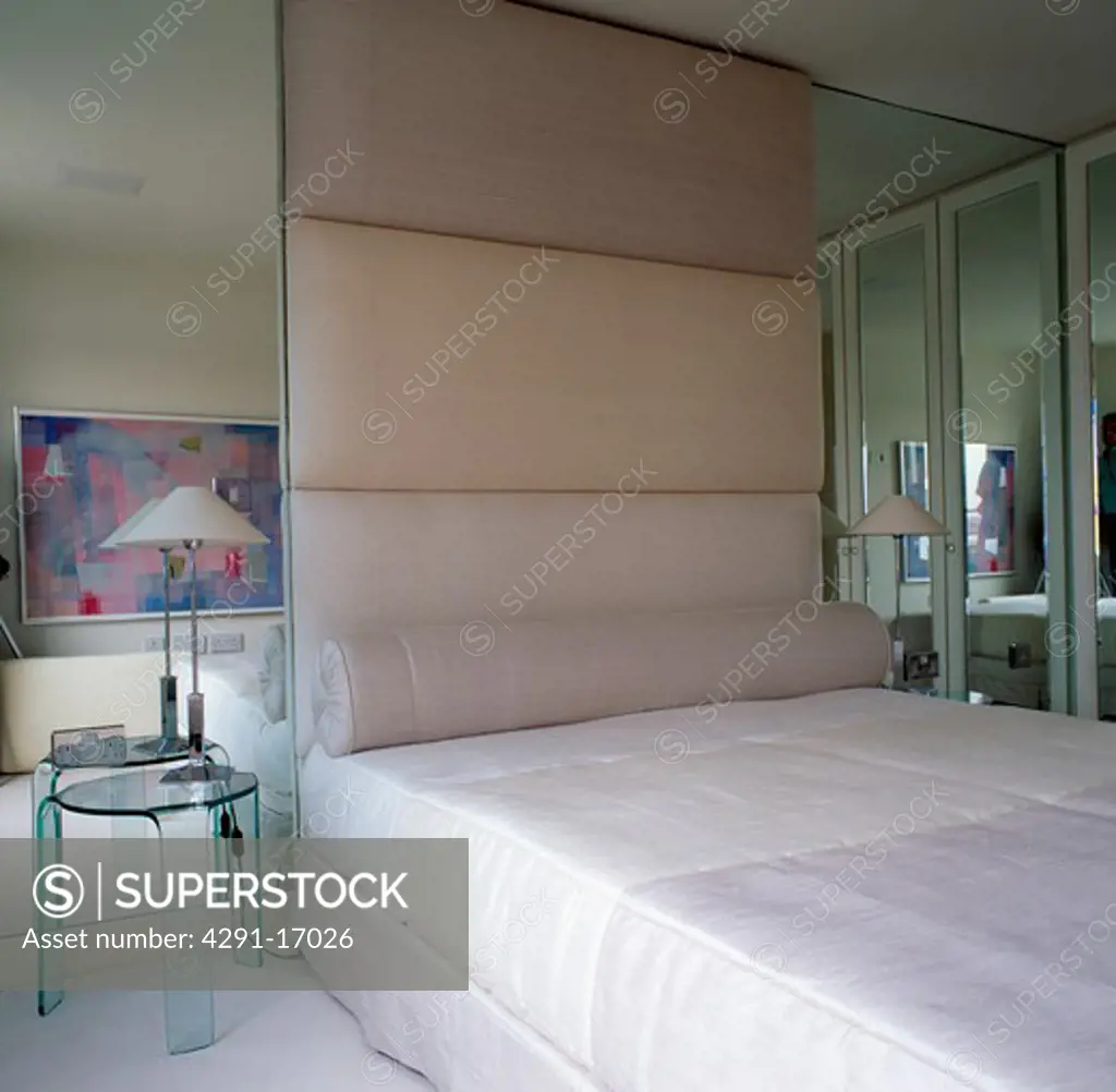 Mirrored wall beside bed below cream upholstered wallin modern city bedroom