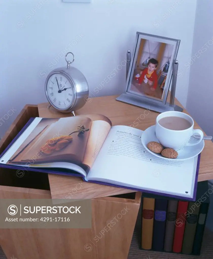 Close-up of cup of tea on book beside alarm clock