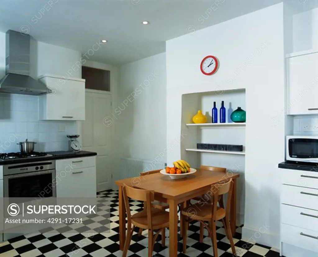 Wooden table and chair in modern kitchen with black and white chequerboard floor
