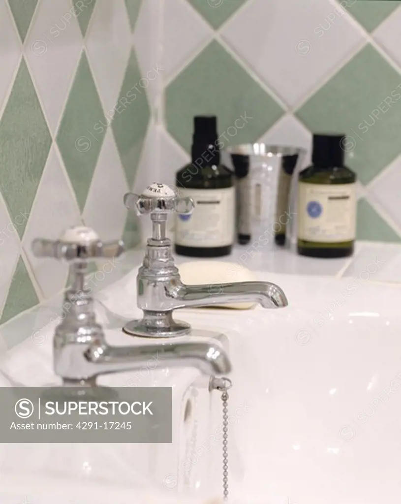 Close up of green and white diamond pattern tiles above chrome taps and toiletries on white bath