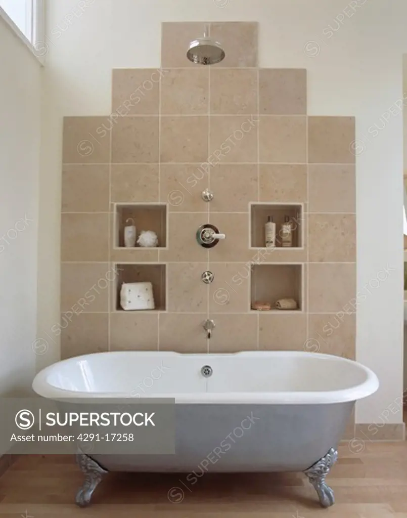Large chrome showerhead above metallic clawfoot bath in modern bathroom with alcove storage on beige tiled wall