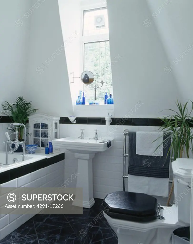 Black toilet seat and white pedestal basin in modern white bathroom with black flooring and black tiled dado