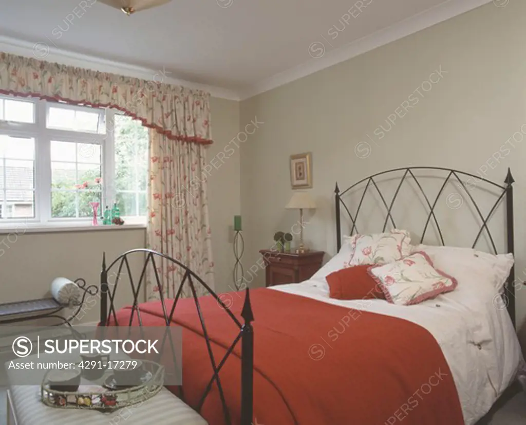 Floral curtains in bedroom with matching cushions and red blanket on iron bed