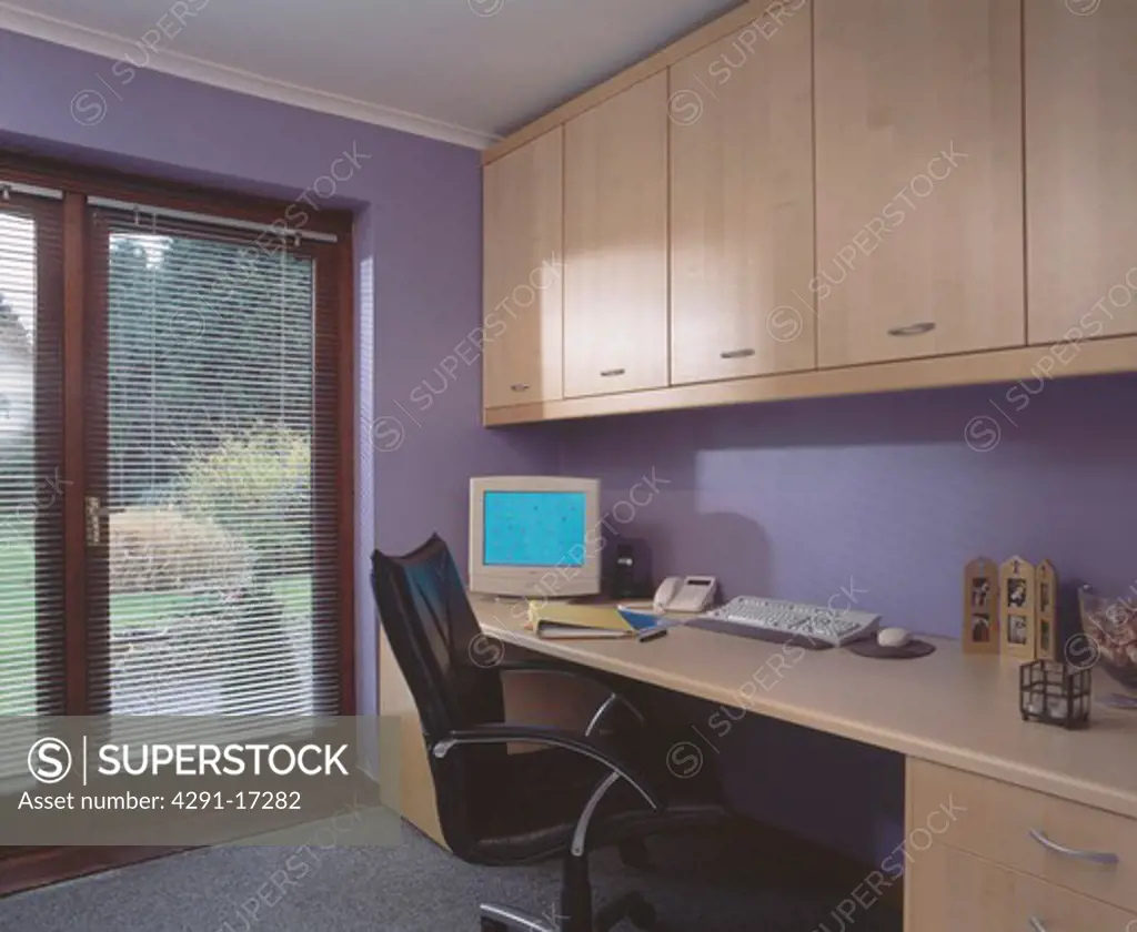 Computer on fitted desk below storage units in modern purple home office