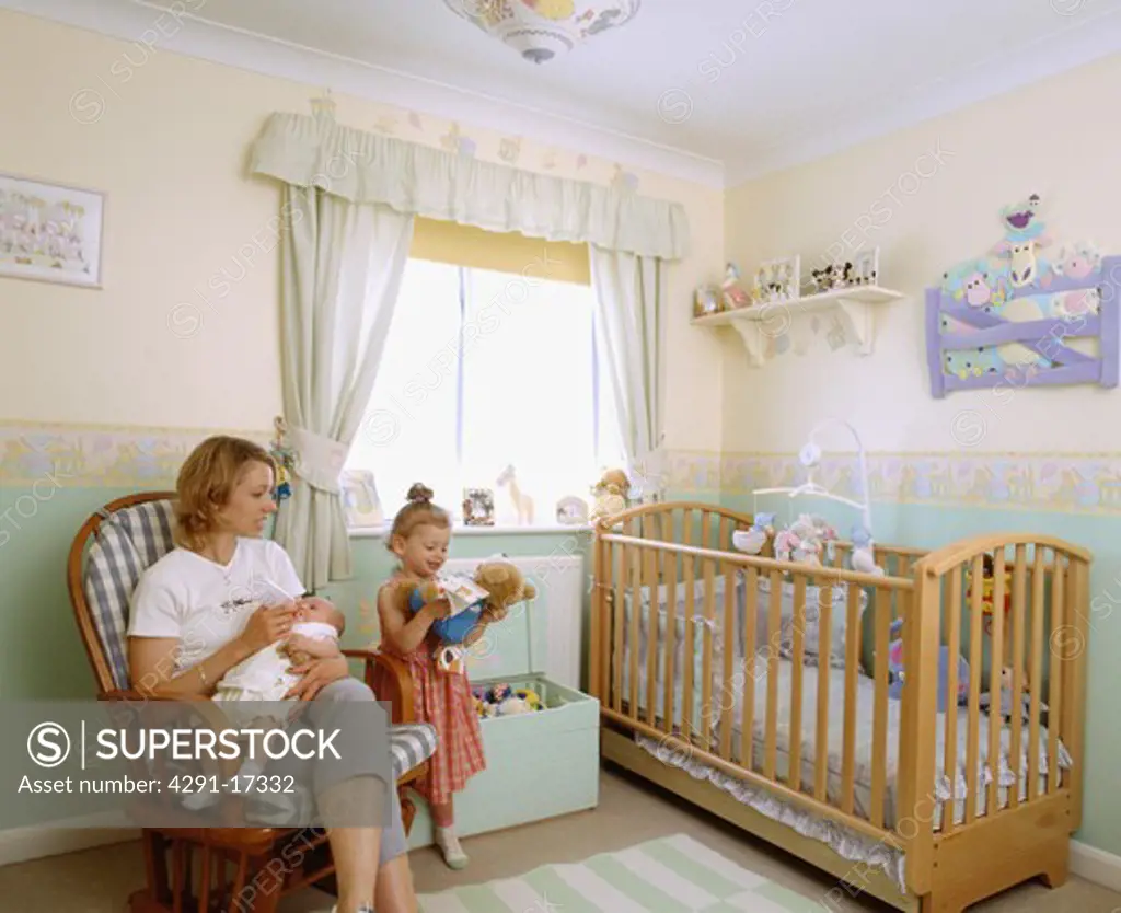 Mother and baby with toddler in childs nursery bedroom with wooden cot